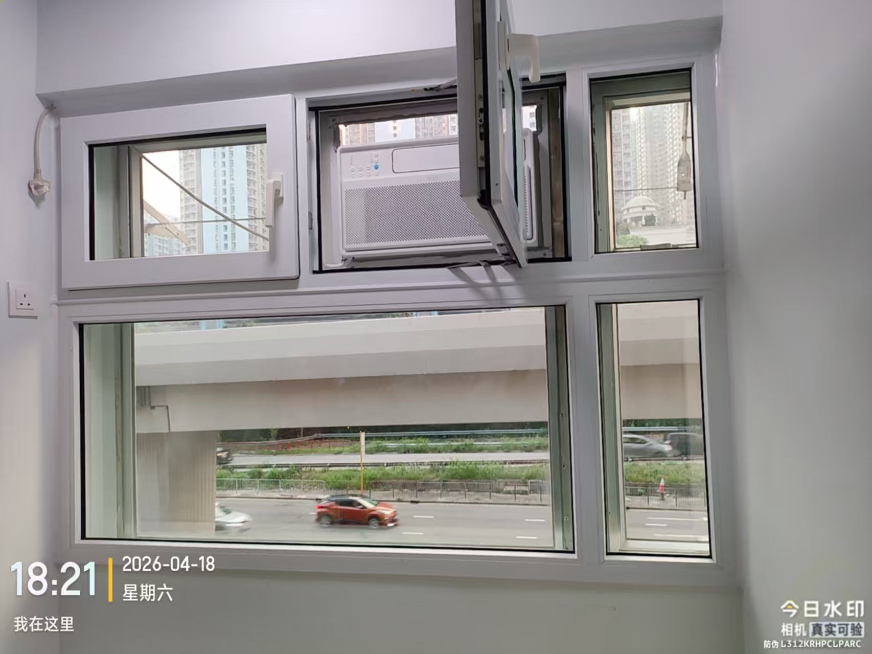 窗式冷氣機前的窗扇開啟狀態,窗外可見道路及高架結構。