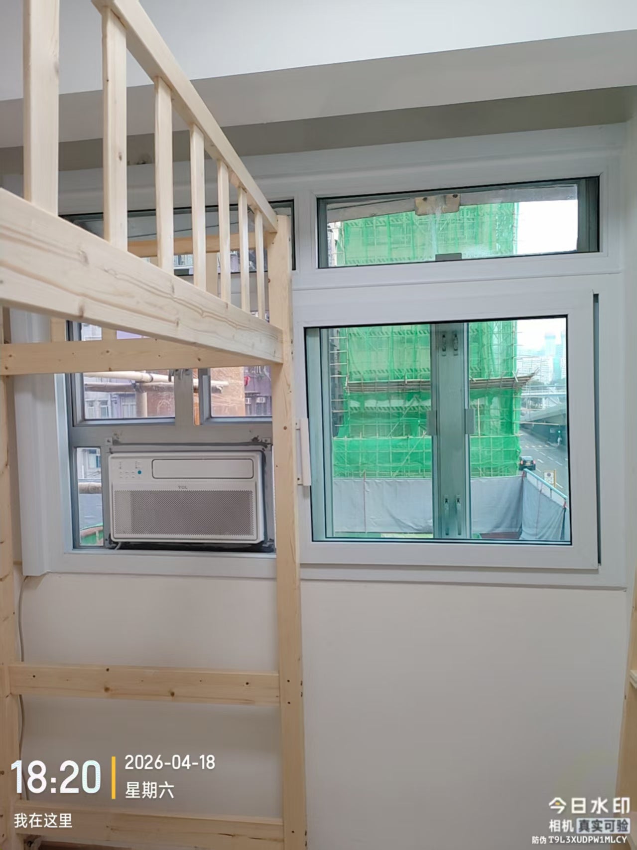 A window assembly and window air conditioner beside a bed frame, with scaffolding visible outside.