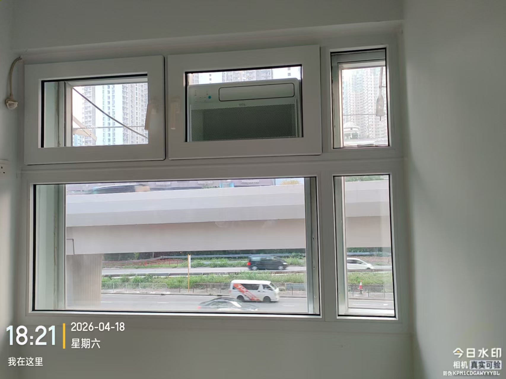 窗式冷氣機前的窗扇關閉狀態，窗外可見道路及高架結構。